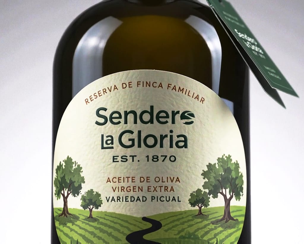 Botella de Sendero la Gloria de cerca: etiqueta redonda con dos olivos y un sendero, y la contraetiqueta verde de cosecha temprana